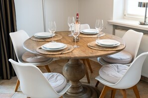 Ein runder Holztisch mit weißen, gepolsterten Stühlen, gedeckt mit Tellern, Gläsern und einer Weinflasche.