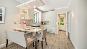 Een moderne keuken met witte kasten, een eethoek met een tafel en stoelen, en uitzicht op het buitenland door een raam.