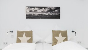 Camera da letto con un letto bianco, due cuscini decorati con stelle, un quadro appeso raffigurante una spiaggia e lampade ai comodini.