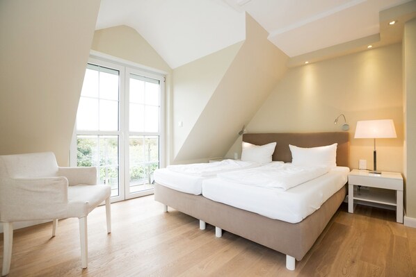 A bedroom with a large bed, a chair, a nightstand, and a window with a view. - Spacious Alster house in Westerland with sauna, garden and modern furnishings (Westerland)