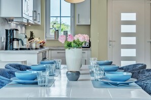A modern kitchen with a dining table set for six, featuring blue bowls and glasses, and a vase with pink flowers. - Spacious Alster house in Westerland with sauna, garden and modern furnishings (Westerland)