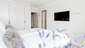 A modern bedroom with a large bed, white wardrobe, and a flat-screen TV mounted on the wall. - Modern vacation apartment with sauna and heated indoor pool in Westerland (Westerland)