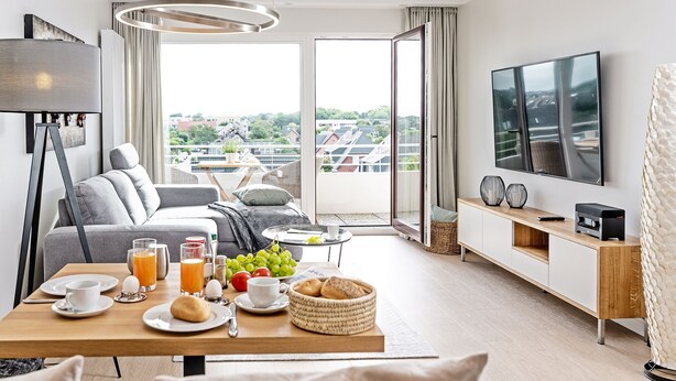 A modern hotel room with a balcony, breakfast setup, and a flat-screen TV. - Modern vacation apartment with sauna and heated indoor pool in Westerland (Westerland)