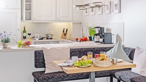 A modern kitchen with white cabinets, a dining area with a bench, and a breakfast setup including fruits, bread, and a coffee maker. - Modern vacation apartment with sauna and heated indoor pool in Westerland (Westerland)