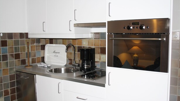 A kitchen with white cabinets, a stainless steel sink, a coffee maker, and an oven. - Comfortable vacation apartment with sauna, garden and parking space in Tinnum (Tinnum)