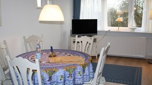 A dining area with a round table, chairs, a television, and a window with curtains. - Comfortable vacation apartment with sauna, garden and parking space in Tinnum (Tinnum)