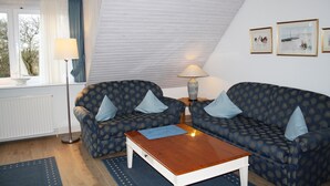 A cozy living room with two patterned sofas, a wooden coffee table, and a floor lamp. - Comfortable vacation apartment with sauna, garden and parking space in Tinnum (Tinnum)