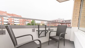 A balcony with two wicker chairs and a small table, overlooking a residential area with brick buildings. - Comfortable apartment with balcony, elevator and parking space in Westerland (Westerland)