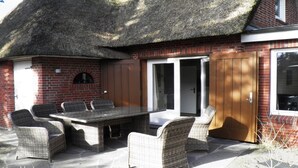Eine Terrasse mit Tisch und Stühlen, eine Ziegelmauer und ein Strohdach.
