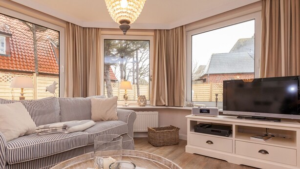 Ein Wohnzimmer mit einem gestreiften Sofa, einem Fernseher und einem großen Fenster mit Vorhängen.