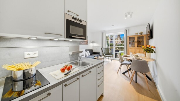 Une cuisine moderne dotée d’un four encastré, un coin repas avec une table et des chaises, et une vue sur l’extérieur.