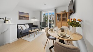 Un salon moderne comprenant un canapé, une table à manger et des chaises, un téléviseur fixé au mur et une fenêtre avec des rideaux.
