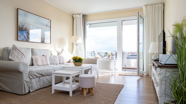 Uma sala de estar moderna com sofá, uma mesinha, planta em vaso e vista da cidade por grandes janelas.