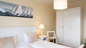 Um quarto com cama, mesa de cabeceira, cadeira, guarda-roupa e um quadro na parede.