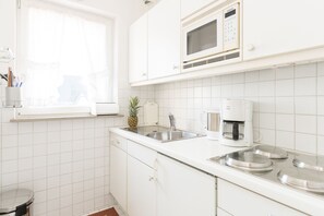 A modern kitchen with white cabinets, a stainless steel sink, a microwave, and a coffee maker. - Comfortable vacation apartment with balcony in Haus Ankerlicht (Westerland)