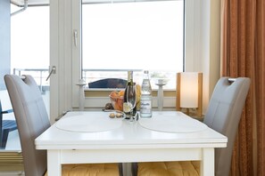 A dining table with two chairs, a bottle of water, a bottle of wine, and a bowl of fruit. - Comfortable vacation apartment with balcony in Haus Ankerlicht (Westerland)