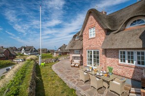 A house with a thatched roof, brick walls, and a stone pathway leading to a patio with outdoor furniture.