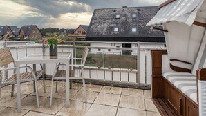 En balkon med et bord og stole, et lille haveområde med tulipaner, og udsigt til omkringliggende huse.