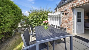 Eine Terrasses mit Tisch und Stühlen, ein Backsteinhaus und ein Hecken.