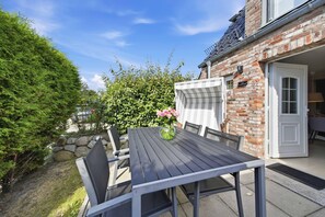 An outdoor patio with a table and chairs, a brick building, and a hedge. - Comfortable penthouse in Westerland with terrace and modern furnishings (Westerland)