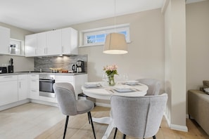 A modern kitchen with white cabinets, a built-in oven, and a dining area with a round table and grey chairs.