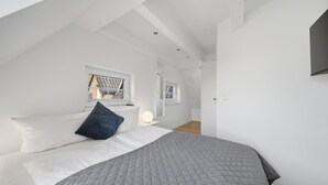 Ein modernes Schlafzimmer mit einem großen Bett, einem Fenster und einem flachbildfernseher an der Wand.