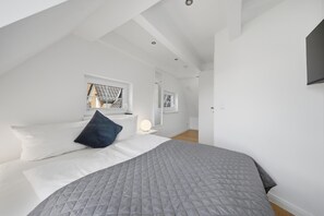 A modern bedroom with a large bed, a window, and a flat-screen TV mounted on the wall. - Comfortable penthouse in Westerland with terrace and modern furnishings (Westerland)