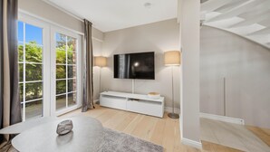 Ein modernes Wohnzimmer mit Flachbildfernseher, einer weißen Unterhaltungseinheit, einem runden Tisch und einer Treppe.