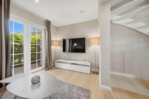 A modern living room with a flat-screen TV, a white entertainment unit, a round table, and a staircase. - Comfortable penthouse in Westerland with terrace and modern furnishings (Westerland)