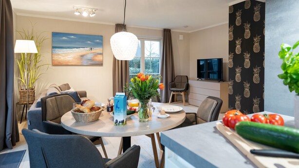 Un salon moderne avec un coin repas, comprenant une grande fenêtre, un téléviseur à écran plat et une table à manger dressée avec de la nourriture et des boissons.