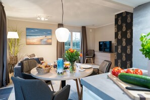 Un salon moderne avec un coin repas, comprenant une grande fenêtre, un téléviseur à écran plat et une table à manger dressée avec de la nourriture et des boissons.