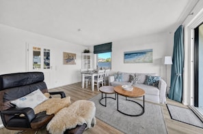 Ein modernes Wohnzimmer mit einer Ledersofa, einem weißen Esstisch und Meerblick durch ein großes Fenster.