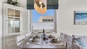 En matplats med ett bord dukat för fyra personer, ett skåp med glasdörrar, ett fönster med utsikt över en byggnad och en tavla på väggen.