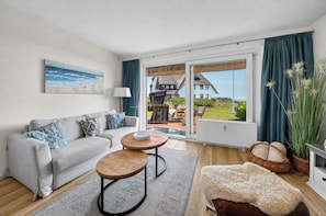 Ein modernes Wohnzimmer mit einer Couch, zwei runden Tischen, einem flauschigen Teppich und Blick auf ein Haus und Garten durch eine Glastür.
