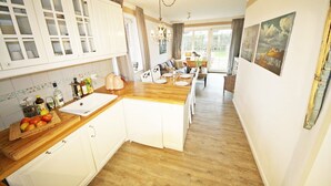 Eine Küche mit weißen Schränken, einer Holz Arbeitsplatte und einem Spülbecken. Durch das Fenster ist eine Essecke mit Tisch und Stühlen zu sehen.