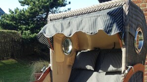 Ein einzigartiger, im Vintage-Stil gestalteter Sessel mit rundem Fenster und Streifenmuster, platziert auf einem Kiesgrund.