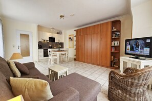 A modern living room with a sofa, a dining table, and a kitchen in the background. - Cozy vacation apartment with swimming pool and sauna in Haus Ornum in Westerland (Westerland)