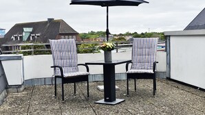 En takterrass med två stolar och ett bord, ett parasoll och en vas med blommor.