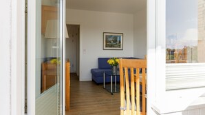 Ein Zimmer mit Holzboden, einem blauen Sofa, einem Glastisch mit Blumenvase und einem Gemälde an der Wand.