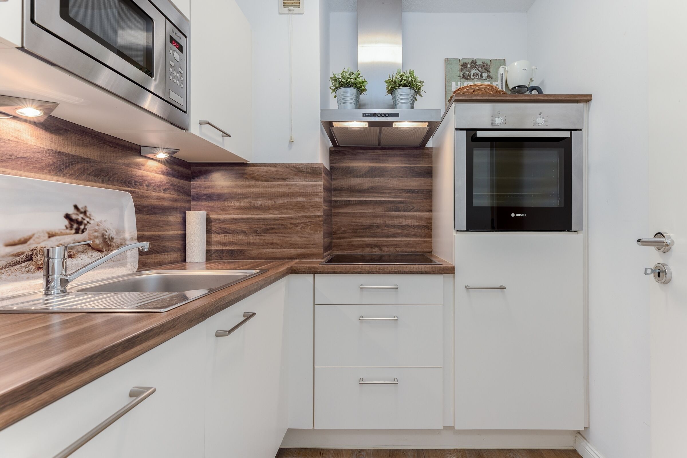A modern kitchen with a built-in oven, stainless steel appliances, wooden countertops, and white cabinetry.