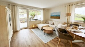 Um quarto espaçoso com uma cama grande, uma mesa de jantar com cadeiras, um sofá e vista para o exterior pelas amplas janelas.
