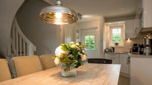 Ein Esstisch mit Blumen in einer Vase, einer Chandelieber und Blick auf den Küchen- und Essbereich.