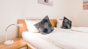 A neatly made bed with white linens and two decorative pillows, a white desk lamp, and a wooden nightstand. - Modern 2-room apartment in a quiet location in Wenningstedt (Wenningstedt)