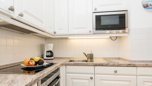 A modern kitchen with white cabinets, a built-in oven, a microwave, a granite countertop, and a fruit bowl. - Modern 2-room apartment in a quiet location in Wenningstedt (Wenningstedt)