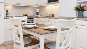 A modern kitchen with white cabinetry, a wooden dining table, and two white chairs. - Modern 2-room apartment in a quiet location in Wenningstedt (Wenningstedt)