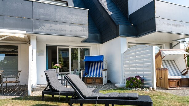 A modern house with a covered patio area featuring two lounge chairs and a small table. - Modern 2-room apartment in a quiet location in Wenningstedt (Wenningstedt)