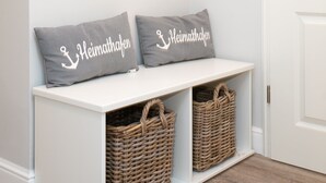 A white bench with two grey pillows, each with "Heimathafen" text, and two wicker baskets underneath. - Comfortable house in Westerland with terrace & garden (Westerland)