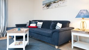 A living room with a dark blue sofa, a white side table, a lamp, and a framed picture on the wall. - Comfortable house in Westerland with terrace & garden (Westerland)