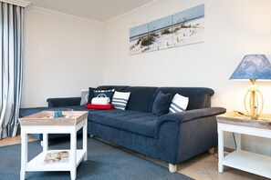 A living room with a dark blue sofa, a white side table, a lamp, and a framed picture on the wall. - Comfortable house in Westerland with terrace & garden (Westerland)