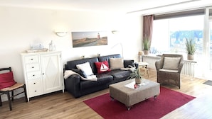 A living room with a black sofa, a white cabinet, a red rug, and a wicker chair. - Bright and cozy vacation apartment directly on the beach crossing in Westerland (Westerland)